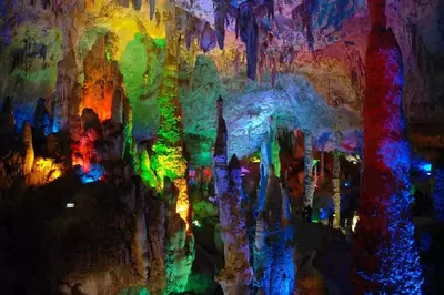Stalactites and stalagmites covered in colorful lights in a cave.