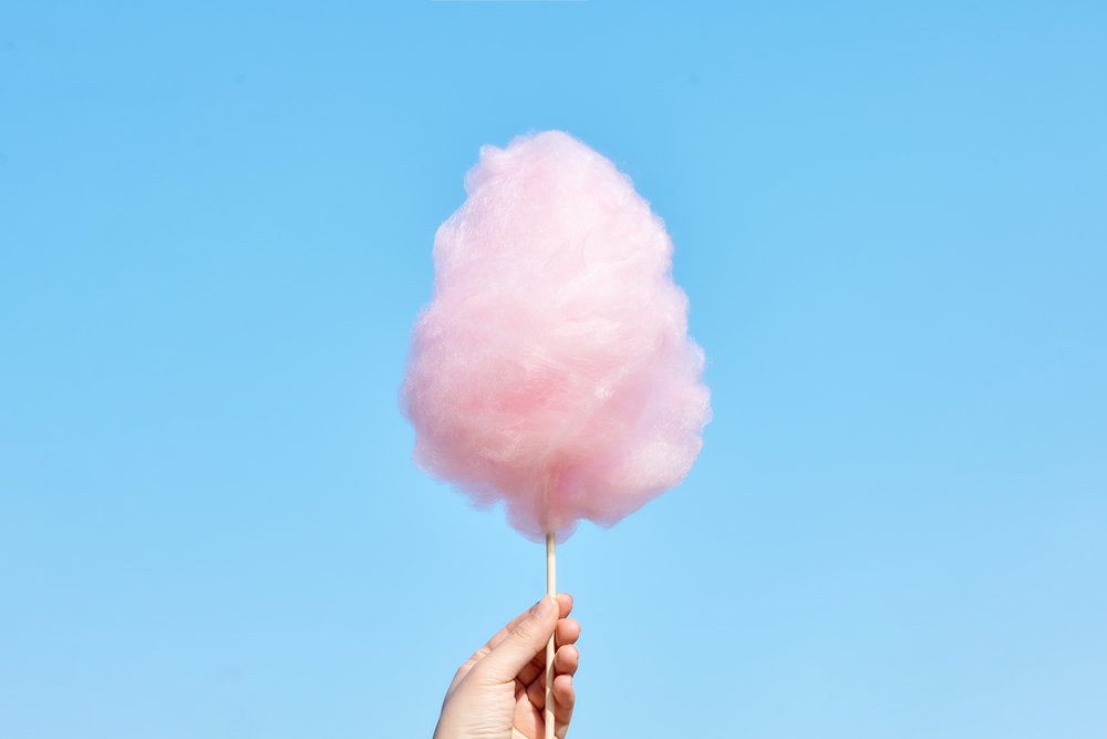 hand holding pink cotton candy on a stick against blue sky